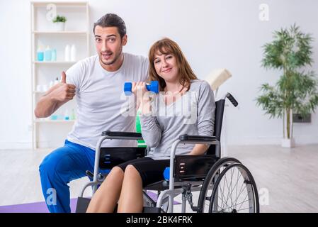 Donna in sedia a rotelle facendo esercizi sportivi con allenatore personale Foto Stock