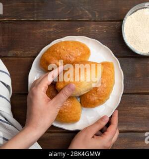 Vista dall'alto delle mani della donna che tengono dei panini farciti (Piroshki) su un tavolo di legno scuro Foto Stock