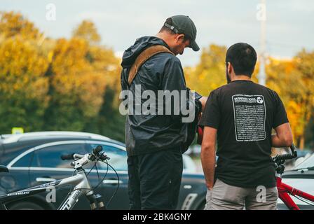 Mosca, Russia - 9 SETTEMBRE 2013: Due uomini con biciclette stanno parlando l'uno con l'altro sullo sfondo di automobili e boschi soliti. Vista posteriore Foto Stock