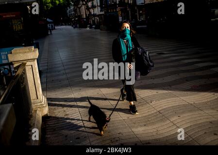 Barcellona, Spagna. 1 maggio 2020 - UNA donna che ricopre il viso con una sciarpa cammina il suo cane vicino alle Las Ramblas vuote a Barcellona. In Spagna l'epidemia continua a rallentare, con 281 morti riferite il venerdì, portando il totale dall'inizio della pandemia a 24,824. Credit:Jordi Boixareu/Alamy Live News Foto Stock