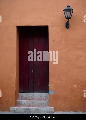 Porta in legno anteriore nella città vecchia cartagena colombia con una lampada sul lato e parete arancione verticale Foto Stock