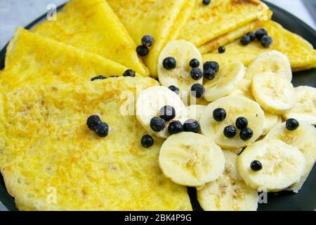 Gustosi pancake con banane e mirtilli su padella nera. Primo piano. Pancake fatti in casa. Pancake colazione cibo Foto Stock