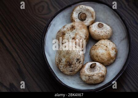 funghi bianchi freschi e sporchi in una ciotola di ceramica con fondo in legno Foto Stock