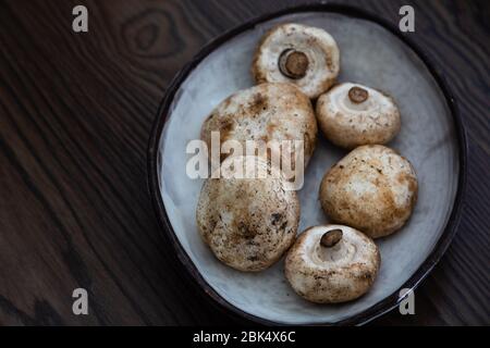 funghi bianchi freschi e sporchi in una ciotola di ceramica con fondo in legno Foto Stock