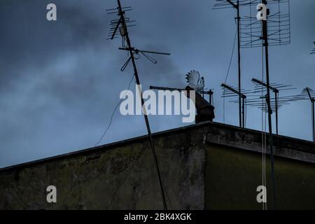 Tra i tetti delle case appare un camino fumatore, il fumo nero esce e invade il cielo. Foto Stock