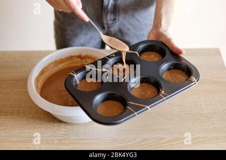 la giovane donna versa l'impasto di cioccolato in stampi per cupcake Foto Stock