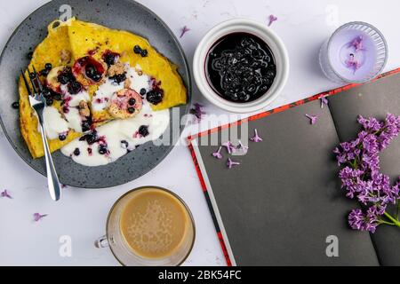 Pancake con frutti di bosco e banane su un piatto grigio con blocco note vuoto su sfondo scuro marable, vista dall'alto. Da sopra, posa piatta, sopra Foto Stock