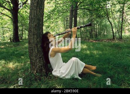 Donna in un abito bianco che gioca il clarinetto in una foresta estiva. Foto Stock