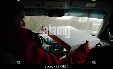 Un addetto alla consegna guida un'auto e tiene una scatola per pizza. Scatto intermedio Foto Stock