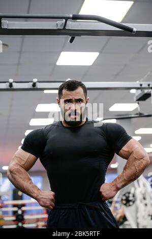 giovane uomo forte con barba che indossa la maglia nera mostrando i suoi muscoli grandi in palestra sportiva Foto Stock