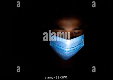 Un giovane uomo blu con maschera chirurgica stava giocando a giochi per smartphone a Dhaka. Foto Stock