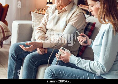 Padre e figlia a casa biblioteca seduta donna aiuta il padre a misurare la pressione sanguigna Foto Stock