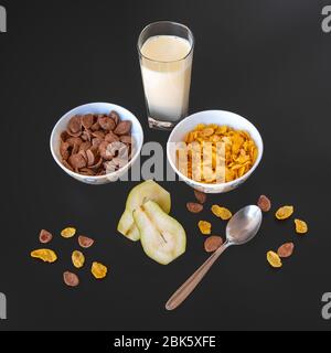 Fiocchi di cioccolato al mais in soffiatura con latte e fette di pera isolate su sfondo grigio nero, una deliziosa e sana colazione a base di cereali dietetici. Foto Stock