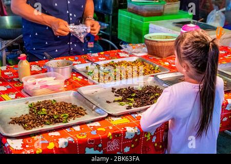 Un piccolo bambino sta comprando alcuni insetti fritti per il cibo al venditore di strada nel sud della Thailandia. Hua Hin, Thailandia, aprile 1.2020 Foto Stock