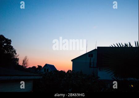 Tramonto nei tropici - un cielo blu scuro con una striscia di rosso tramonto sullo sfondo di case, piante e palme. Viaggio estivo serale turismo caucasico montagna Foto Stock