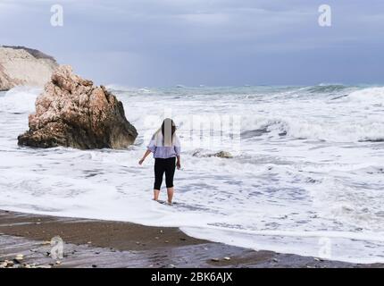 Persona sconosciuta che gode il mare tempestoso con le onde ventose. Luogo di nascita della roccia di Afrodite, costa di Petra tou romiou nella zona di Paphos a Cipro Foto Stock