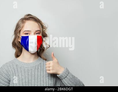 Donna felice in maschera viso tenendo il pollice in su con bandiera nazionale Francia sfondo. Influenza epidemica e protezione del virus concetto Foto Stock