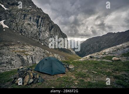 Tenda verde nel grigio mountain valley con nuvoloso nubi di pioggia in Karakol national park, il Kirghizistan Foto Stock