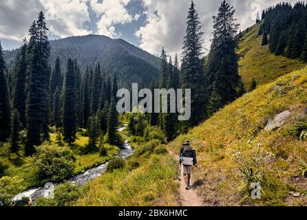 Escursionista con grande zaino è di camminare sulla strada con una vista spettacolare delle montagne e del fiume Foto Stock