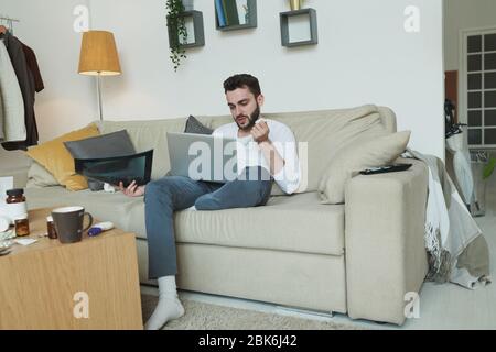 Uomo malato con raggi X seduta sul divano con il laptop in ginocchio e consultare il medico online mentre si è a casa Foto Stock