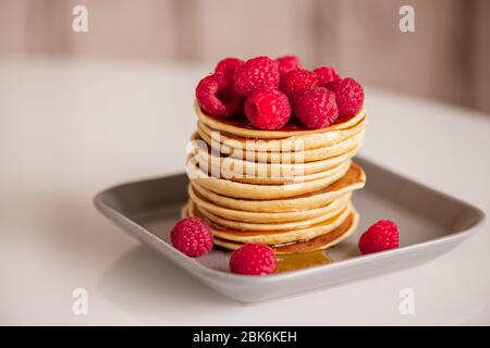 Lamponi freschi e appetitosi sopra una pila di pancake caldi fatti in casa con miele cucinato per colazione al mattino a casa Foto Stock