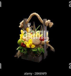 Un regalo unico nella forma di una scatola di legno piena di fiori e frutta su uno sfondo nero. Foto Stock