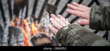 Primo piano dettaglio vista dall'alto della donna che riscalda le mani intorno fuoco fuoco caldo nel camino durante la stagione invernale fredda. Strada urbana all'aperto Foto Stock