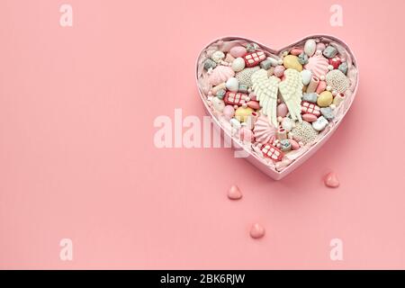 Scatola a forma di cuore riempita con diversi dolci e caramelle fatte a mano su uno sfondo rosa, spazio copia. Foto Stock