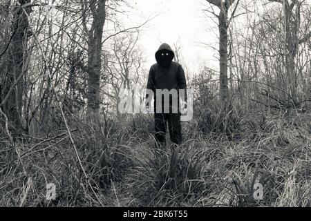 Una figura spaventosa e con cappuccio, con occhi malvagi e spazi neri vuoti dove dovrebbe essere il suo volto, in piedi in una foresta in inverno. Con una modifica vintage. Foto Stock