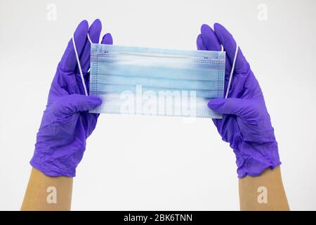 Chiudere la maschera medica monouso nelle mani del medico con guanti di gomma blu Foto Stock