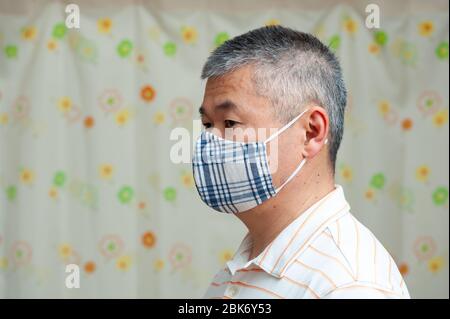 Profilo Vista laterale ritratto di media età Asian uomo che indossa (DIY) maschera in tessuto fatto in casa per la protezione contro il coronavirus (COVID-19). Foto Stock