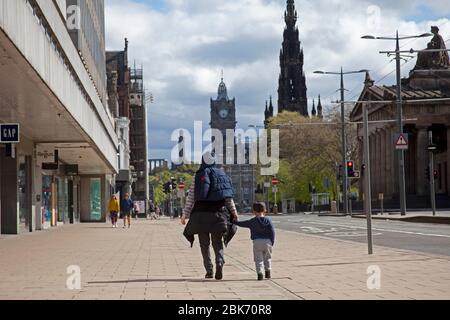 Centro di Edimburgo, Scozia, Regno Unito. 2 maggio 2020. Il quarantesimo giorno del blocco britannico di Coronavirus porta strade e marciapiedi quasi vuoti nella capitale scozzese, con l'occasionale pedone. In tempi normali un sabato mattina avrebbe portato molti pedoni affollati in Princes Street e i negozi e ristoranti George Street e Castle Street dove il parcheggio sarebbe difficile, non oggi in questa mattina di sole si sente spaventosamente eerie.pictured donna e ragazzo a piedi lungo marciapiede ovest a est. Orologio Balmoral con tempo sbagliato. Credit: Arch White/Alamy Live News. Foto Stock