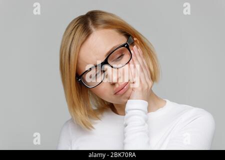 Piangendo giovane donna in occhiali con si sente infelice e depresso, guardando verso il basso, isolato su sfondo grigio. Malinconia, rottura dei rapporti, azione d'amore Foto Stock