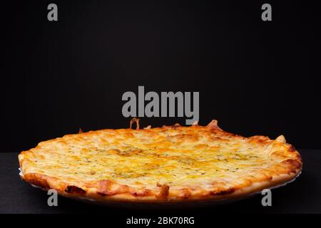 Pizza semplice a quattro formaggi con cresta croccante e tinta giallo dorato studio low key Still Life su sfondo scuro Foto Stock