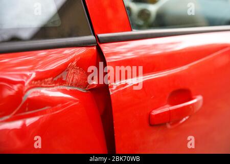 Vettura rossa della portiera danneggiata in caso di incidente con ammaccature profonde, graffi sulle portiere. Concetto di riparazione auto. Foto Stock