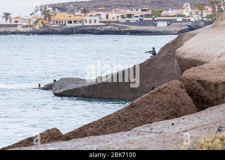 Pescatore Lone sulle rocce durante il covid 19 blocco nella zona turistica di Costa Adeje, Tenerife, Isole Canarie, Spagna Foto Stock