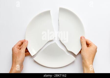 Vista dall'alto delle mani dell'uomo che tengono un piatto bianco rotto. Metafora per il divorzio, i rapporti, le amicizie, crack nel matrimonio. L'amore è andato. Isolato su whi Foto Stock