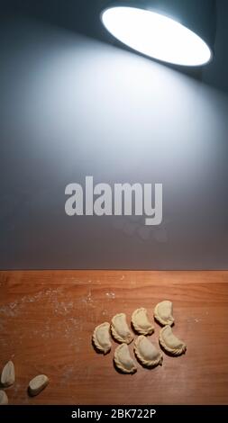 Gnocchi giacenti sul piano di cottura in legno vicino alla parete illuminando da lanterna, ravioli crudi preparati e pronti per la cottura prima dell'ebollizione Foto Stock