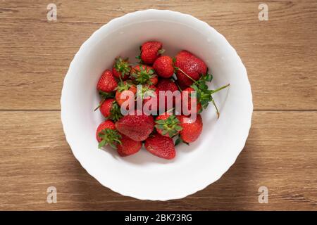 Fragole appena raccolte in un bagno bianco posto su un tavolo di legno, vista dall'alto; frutta pulita e lavata, colazione a scelta sana Foto Stock