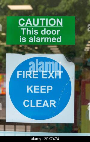 una vista ravvicinata di un cartello di avvertenza e di uscita antincendio sul finestrino di un negozio Foto Stock