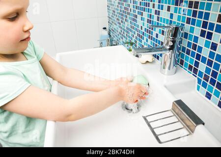 Il bambino lava diligentemente le mani con acqua e sapone eseguendo le misure protettive di base contro la diffusione del coronavirus COVID-19 desease Foto Stock
