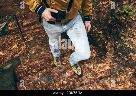 Giovane durante il viaggio. Basso sezione di fotografo con fotocamera a piedi sul sentiero. Foto Stock