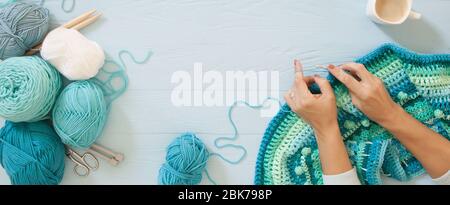 Le mani delle donne sono grandi. Donna crochets. Filati di colore verde, turchese, acquamarina e blu. Legno blu lungo sfondo. Foto Stock