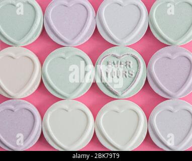 Un'immagine dei dolci dei cuori dell'Amore con la caramella in una fila ed il messaggio dell'amore mai il vostro che si levano in piedi fuori fra i dolci vuoti con lo spazio della copia Foto Stock