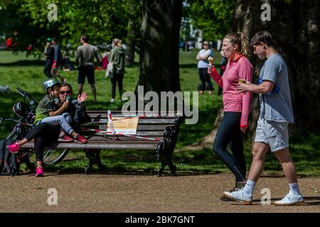 Londra, Regno Unito. 02 maggio 2020. Felice di mangiare gelato, ma anche rompere le regole di non seduta, come i camminatori cane chiacchierare, distanziati, in background - è il dilema chiaro di allentamento blocco. Il caffè vicino al banchet chiuso è ora aperto, per bevande e gelati, con un sistema a senso unico e distanza sociale. Clapham Common è abbastanza occupato, come il sole è fuori ed è più caldo. Il blocco continua per l'epidemia di Coronavirus (Covid 19) a Londra. Credit: Guy Bell/Alamy Live News Foto Stock