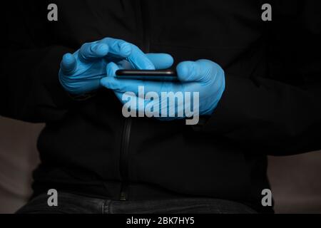 Uomo che indossa guanti protettivi blu DPI utilizzando uno smartphone touchscreen durante l'epidemia di Coronavirus Covid-19. Concetto per la tecnologia durante la pandemia, vi Foto Stock