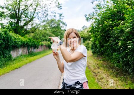 Una donna toglie la maschera in un parco sulla strada verde Foto Stock