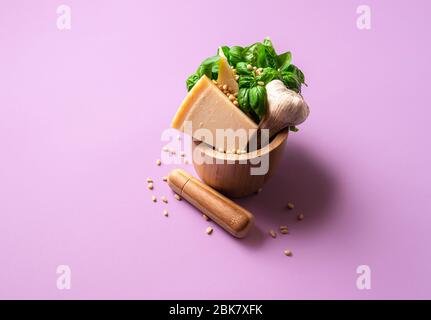 Pesto ingredienti in un mortaio di legno su sfondo viola. Basilico fresco, parmigiano, aglio e pinoli per la preparazione del pesto. Salsa di pasta. Foto Stock