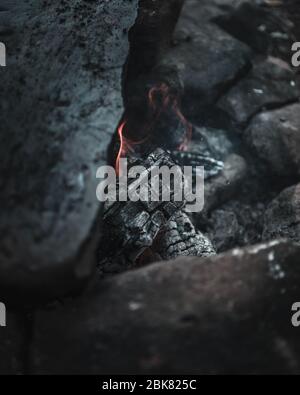 Moody Vibe con Smoldering Embers e una fiamma nel Roccia fuoco Pit Foto Stock