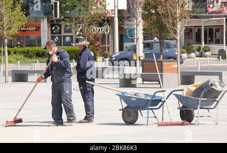 Belgrado, Serbia - 24 aprile 2020: Lavoratori edili riempendo i giunti in granito con sabbia utilizzando ginestra lunga, pavimentazione stradale finitura, carriola Foto Stock